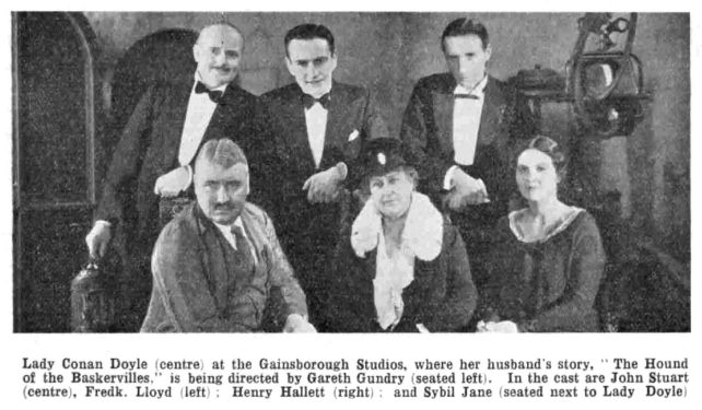 Lady Conan Doyle Visits Gainsborough : Lady Conan Doyle (centre) at the Gainsborough Studios, where her husband's story, "The Hound of the Baskervilles," is being directed by Gareth Gundry (seated left). In the cast are John Stuart (centre), Fredk. Lloyd (left); Henry Hallett (right); and Sybil Jane (seated next to Lady Doyle) (The Bioscope, 4 february 1931, p. 18).